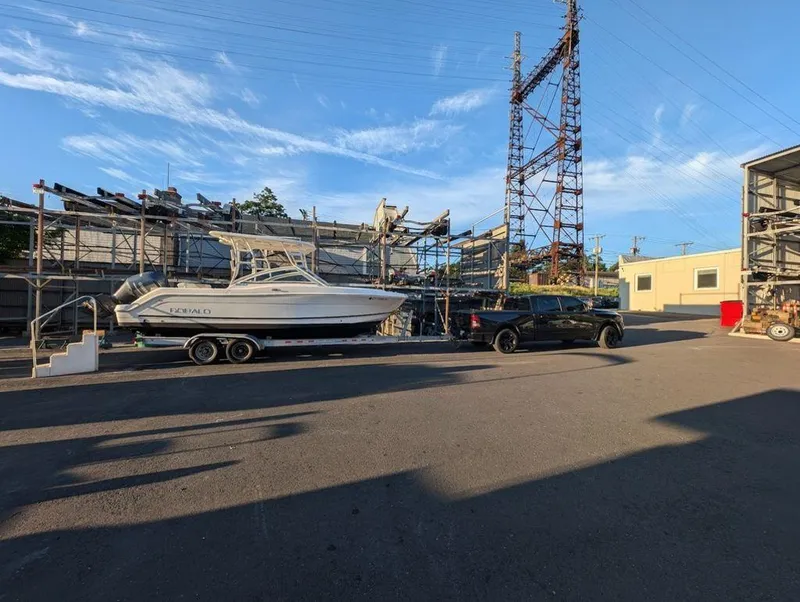 Slide: The Image of 2018 Robalo R247 Dual Console boat on trailer beside black truck in industrial area. - 7