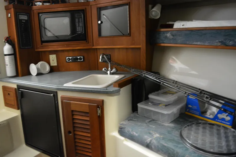 Slide: The Image of 2004 Carolina Classic 28 boat interior with kitchenette, sink, microwave, and fishing gear. - 36