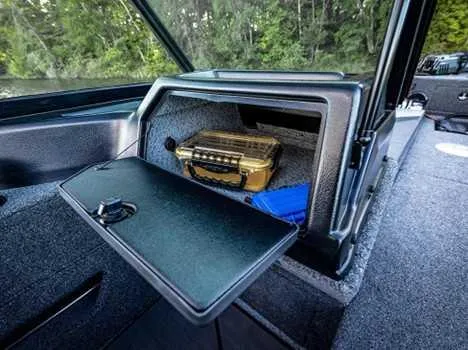 Slide: The Image of 2026 Lund 2075 IMPACT XS boat storage compartment with gear and forest backdrop. - 17