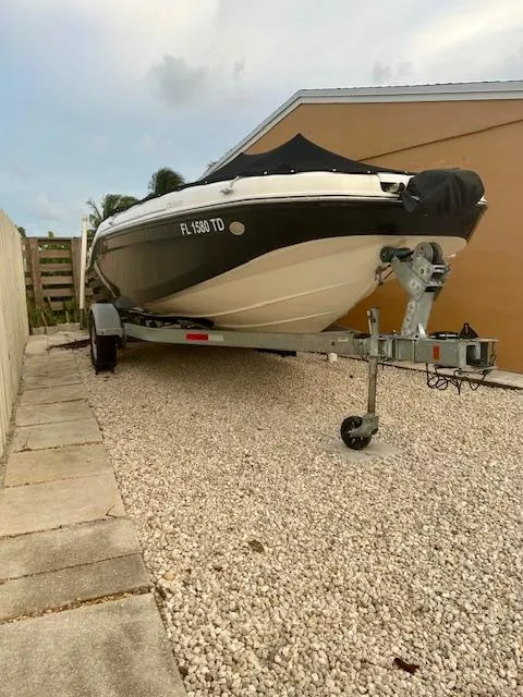 Slide: The Image of 2022 Bayliner DX2000 boat on trailer, parked on gravel beside a house. - 2