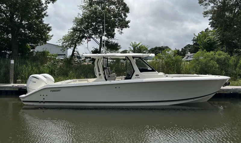 The Image of 2026 Pursuit S 328 boat docked on calm water, surrounded by lush greenery. - 0