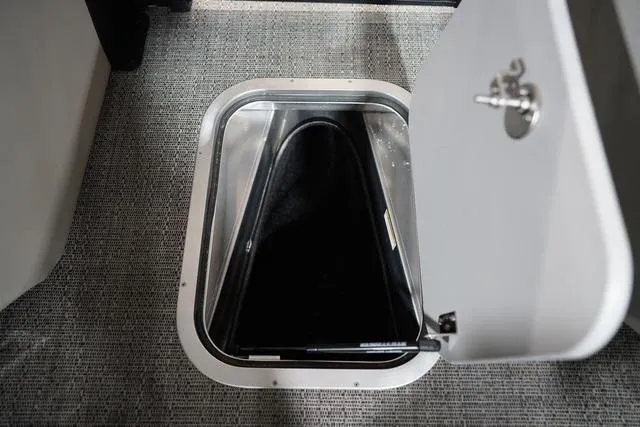 Slide: The Image of Open storage compartment on 2025 Barletta Corsa 23UC boat, featuring a secure latch and carpeted interior. - 7