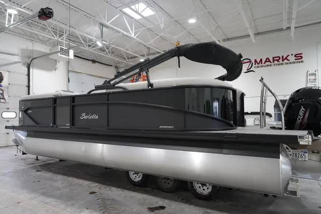 Slide: The Image of 2025 Barletta Boats C22QC pontoon in showroom, sleek design, black exterior, triple-axle trailer. - 5