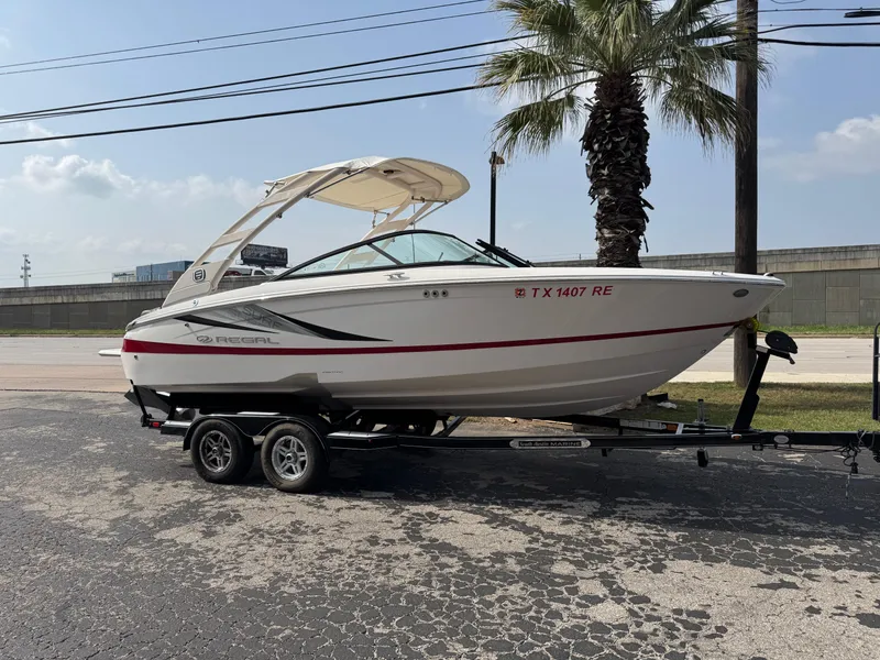 Slide: The Image of 2020 Regal LS2 Surf boat on trailer, parked near palm tree, sunny day. - 0