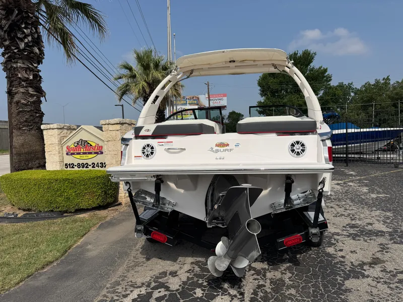 Slide: The Image of 2020 Regal LS2 Surf boat, rear view, parked outdoors near palm trees and signage. - 2