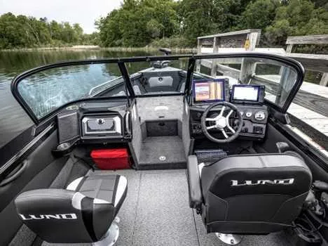Slide: The Image of 2026 Lund 2075 Tyee boat interior with modern dashboard and seating, docked by a lake. - 1