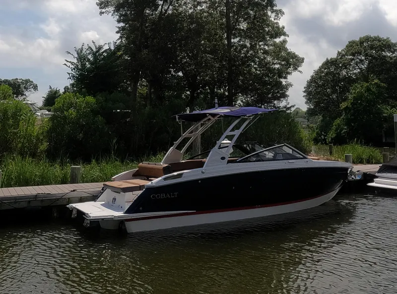 Slide: The Image of 2026 Cobalt R6 boat docked by lush greenery under a cloudy sky. - 2