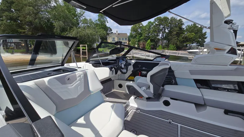 Slide: The Image of 2022 Correct Craft Super Air Nautique G23 interior with modern seating and steering, docked by a lake. - 19