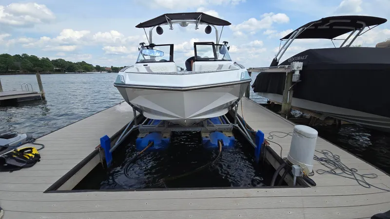 Slide: The Image of 2022 Correct Craft Super Air Nautique G23 boat on a dock lift by the lake. - 2
