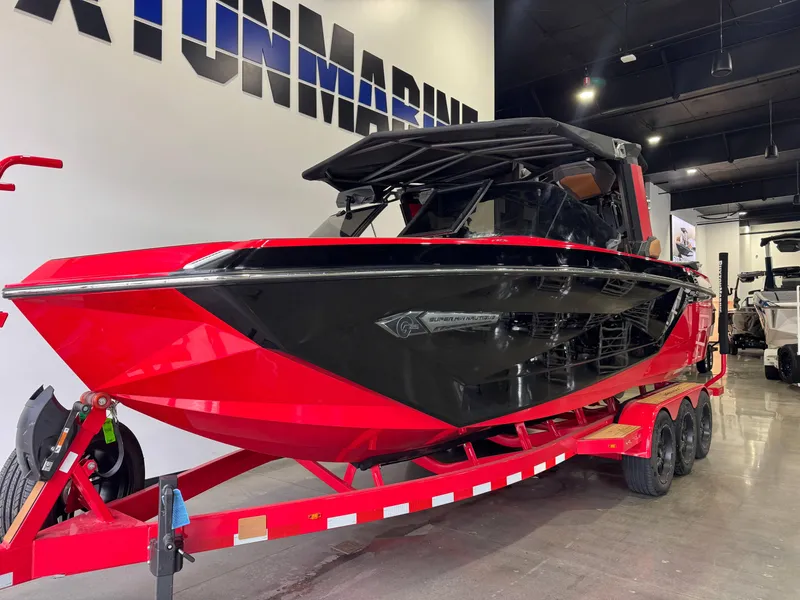 Slide: The Image of 2024 Nautique Super Air Nautique G25 boat in showroom, red and black design on trailer. - 2