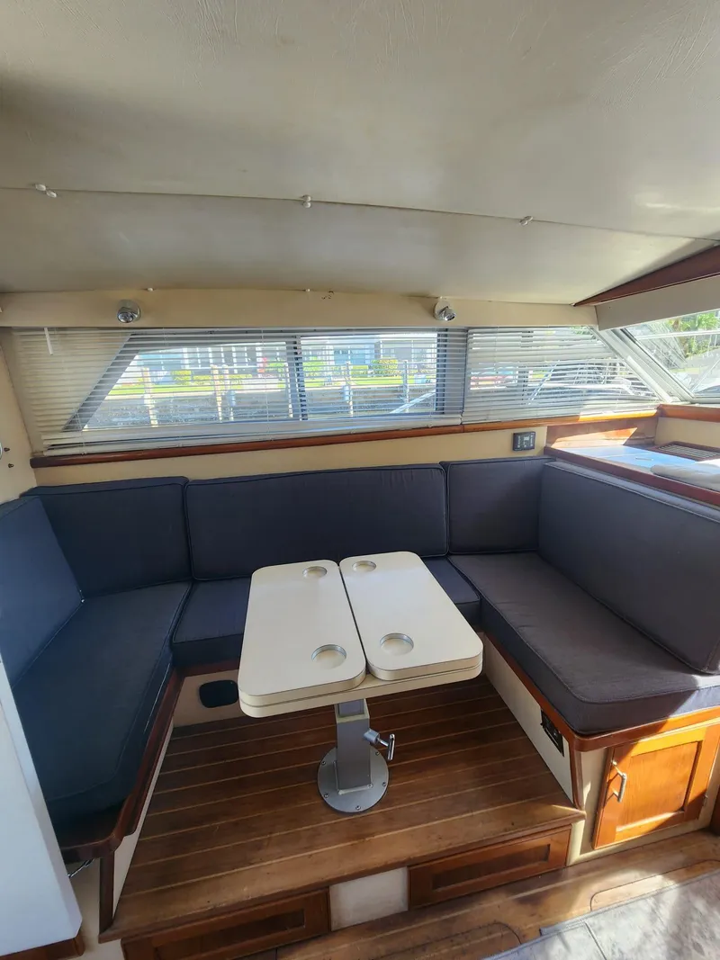 Slide: The Image of 1984 Bertram 30 Express interior with cozy seating and table, featuring wood accents and ample windows. - 12
