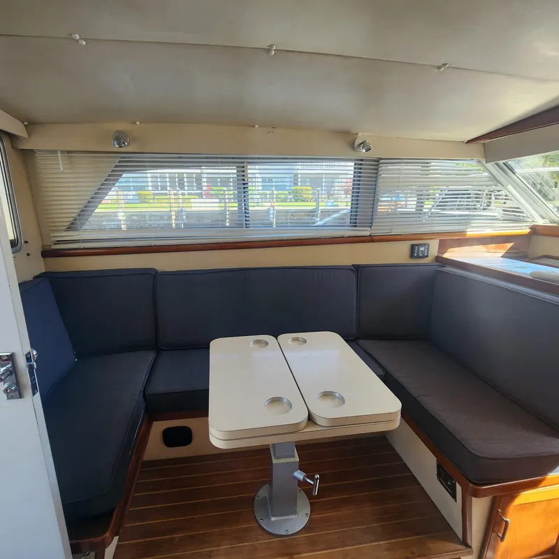 Slide: The Image of 1984 Bertram 30 Express interior with seating and table, featuring wood flooring and large windows. - 8