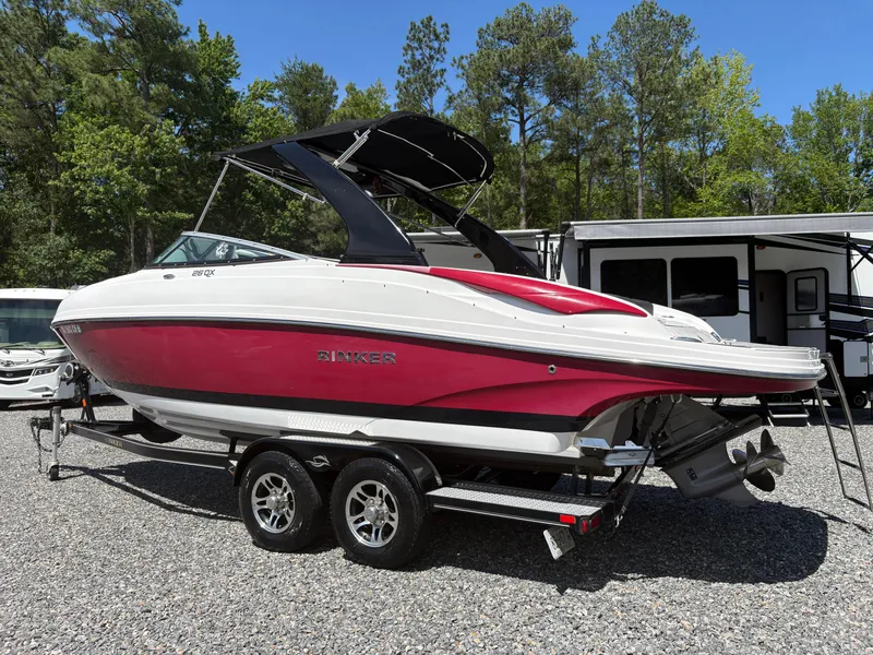 Slide: The Image of 2018 Rinker 26QX BR boat on trailer, red and white, parked outdoors. - 2