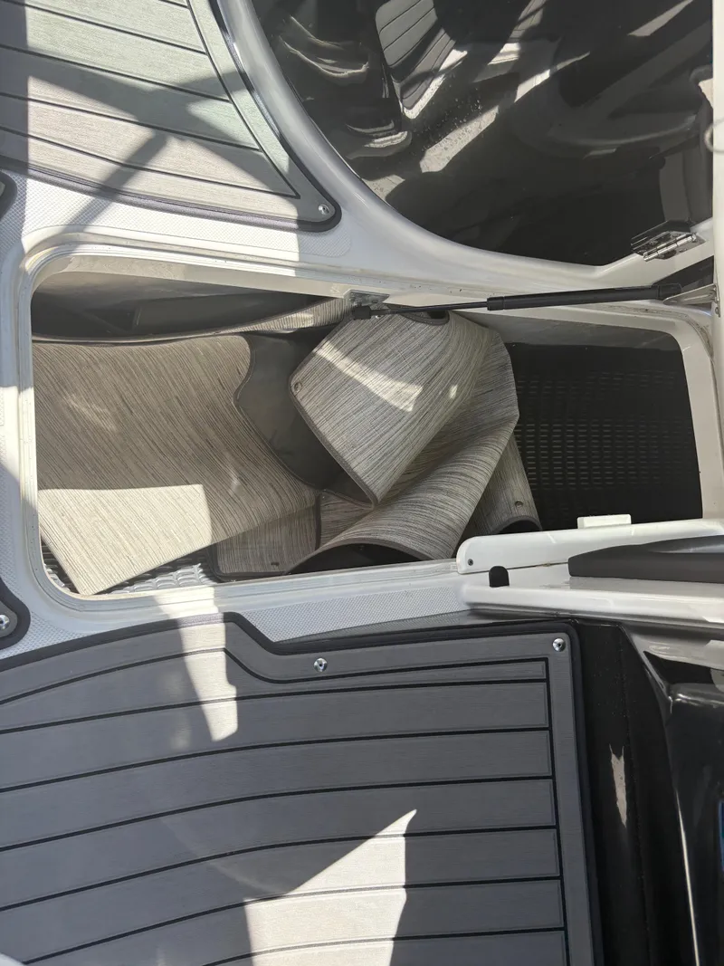 Slide: The Image of 2018 Rinker 26QX BR boat interior storage compartment with rolled carpet. - 26