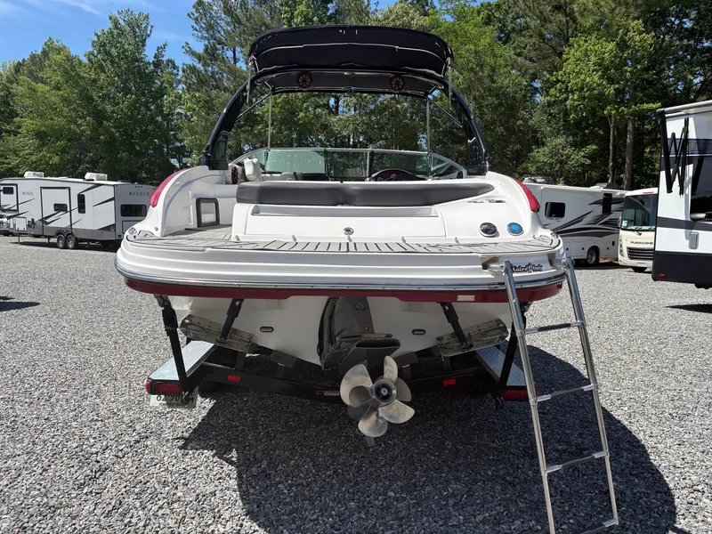 Slide: The Image of 2018 Rinker 26QX BR boat rear view with ladder, parked on gravel lot. - 3