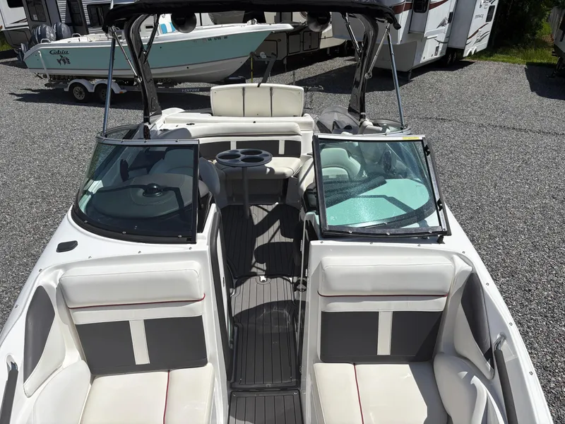 Slide: The Image of 2018 Rinker 26QX BR boat interior with seating and windshield, parked on gravel. - 32