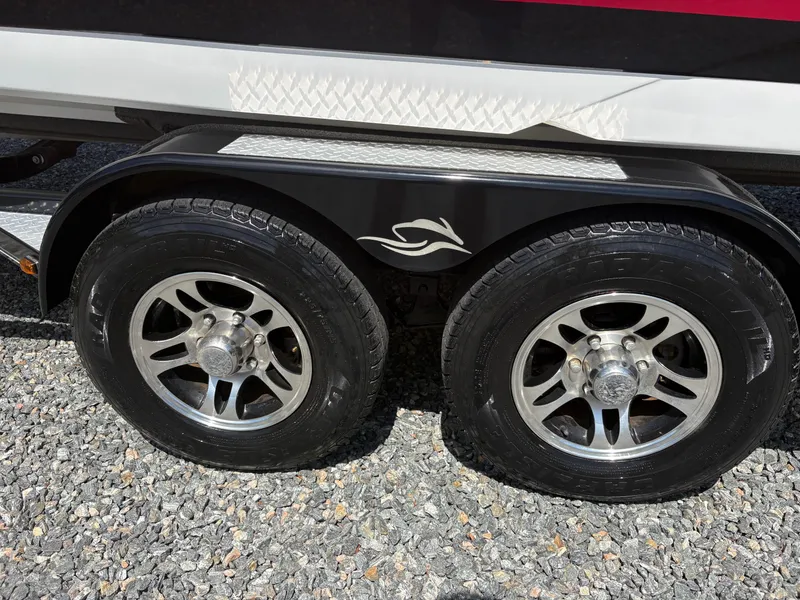 Slide: The Image of Trailer wheels of a 2018 Rinker 26QX BR boat on gravel surface. - 33