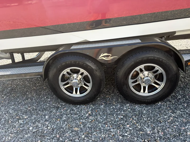 Slide: The Image of Trailer wheels of a 2018 Rinker 26QX BR boat on gravel surface. - 34