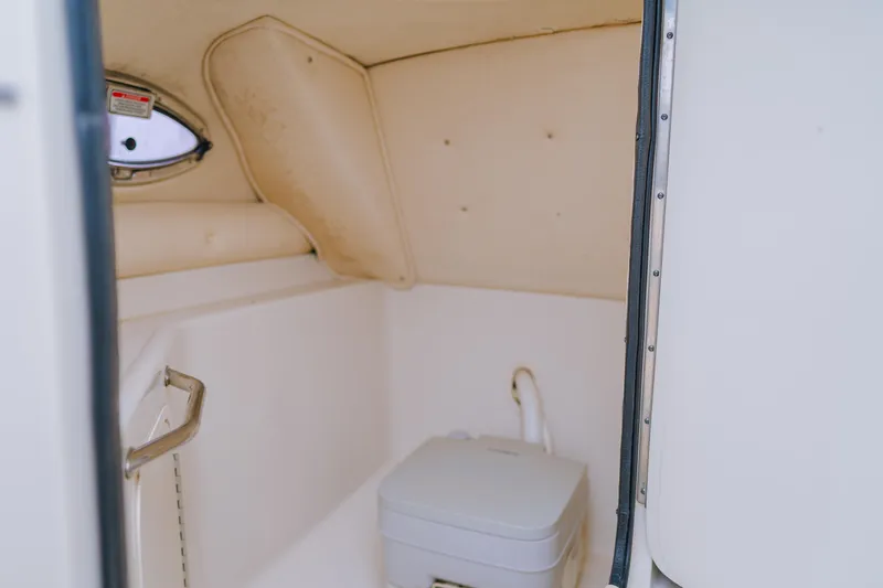 Slide: The Image of 2003 Sea Ray 240 Sundeck interior with compact marine toilet and porthole. - 5