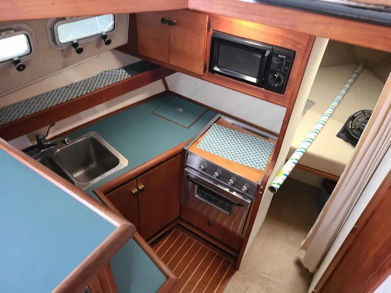 Slide: The Image of 1989 Bayliner 3255 Avanti interior with kitchen, sink, stove, microwave, and cozy sleeping area. - 13