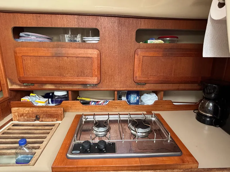 Slide: The Image of Compact kitchen in a 1990 Hunter 33.5 sailboat with stove, wooden cabinets, and coffee maker. - 47