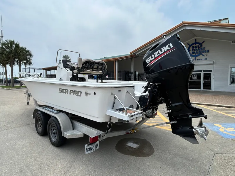 Slide: The Image of 2020 Sea Pro 228 Bay boat on trailer with Suzuki outboard motor, parked near a building. - 1