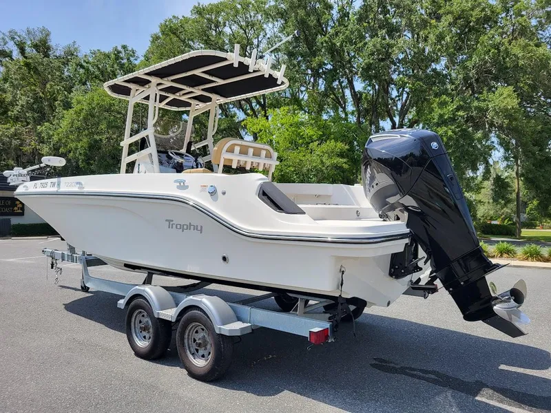 Slide: The Image of 2024 Bayliner Trophy T22CC boat on trailer, parked outdoors with trees in background. - 3