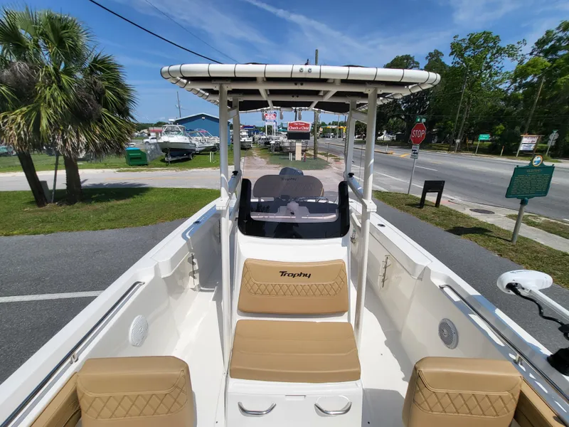 Slide: The Image of 2024 Bayliner Trophy T22CC boat with tan seating, parked near a road and palm trees. - 6