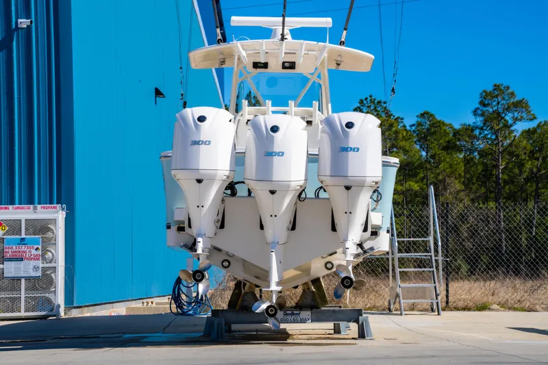 Slide: The Image of 2019 Regulator 34 boat with triple outboard engines, parked near a blue building. - 2