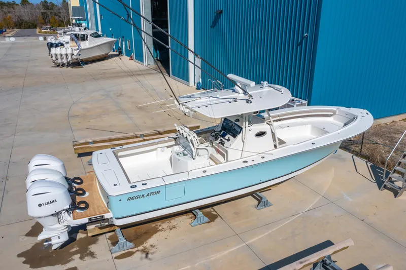Slide: The Image of 2019 Regulator 34 boat with triple Yamaha engines, docked near blue warehouse. - 27