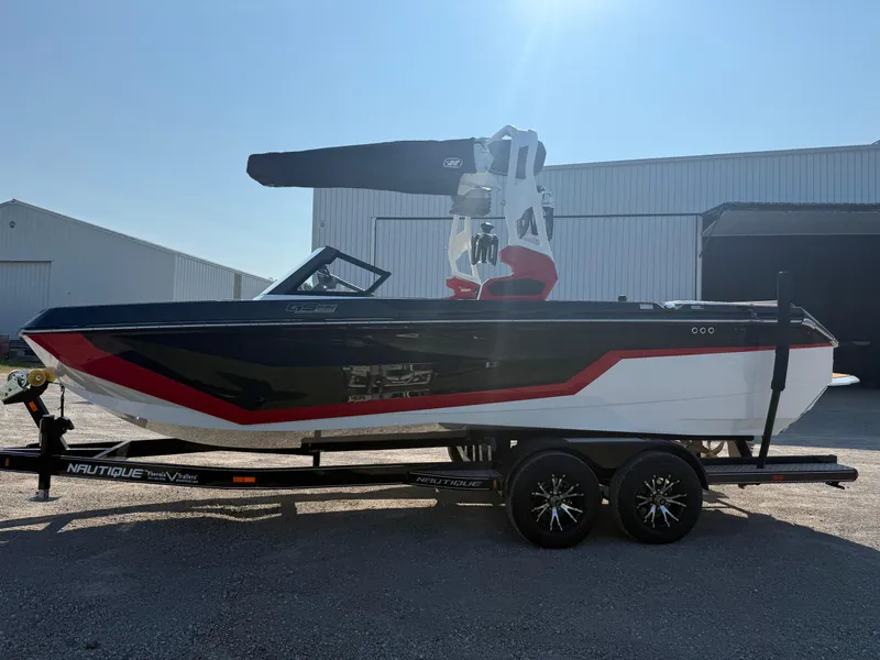 Slide: The Image of 2025 Nautique Super Air Nautique GS22 boat on trailer, black and red design, parked outdoors. - 1