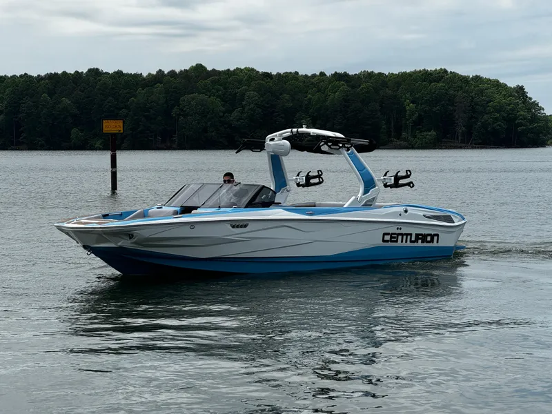Slide: The Image of 2025 Centurion NV233 boat cruising on a lake with forested shoreline. - 5