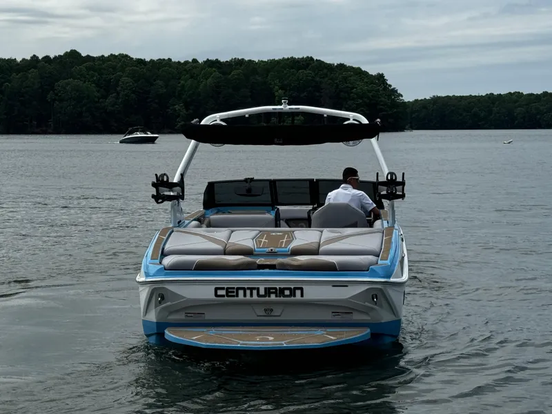 Slide: The Image of 2025 Centurion NV233 boat on a lake, rear view with lush forest background. - 6