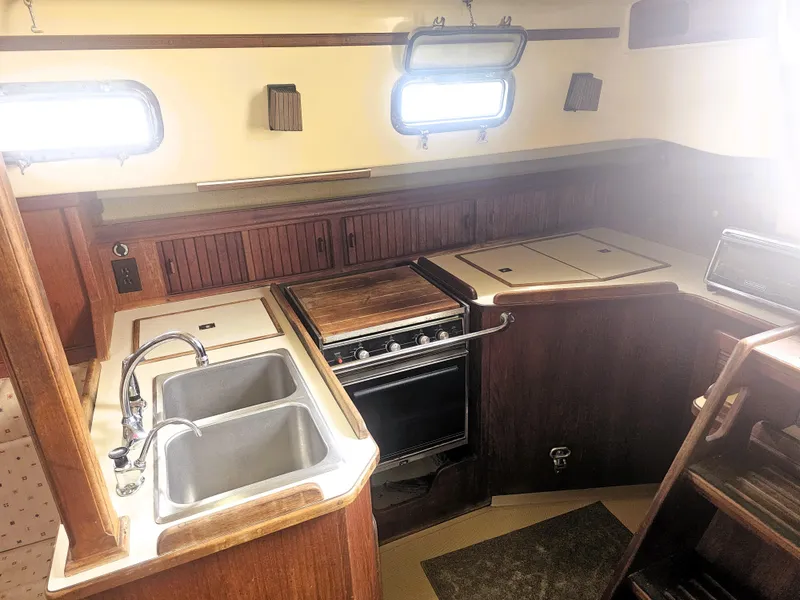 Slide: The Image of 1990 Island Packet 35 yacht kitchen with dual sinks, stove, and wooden cabinetry. - 4