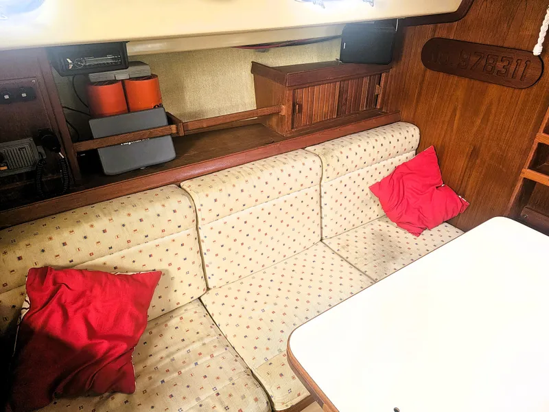 Slide: The Image of Interior of 1990 Island Packet 35 sailboat with cushioned seating and red pillows. - 6