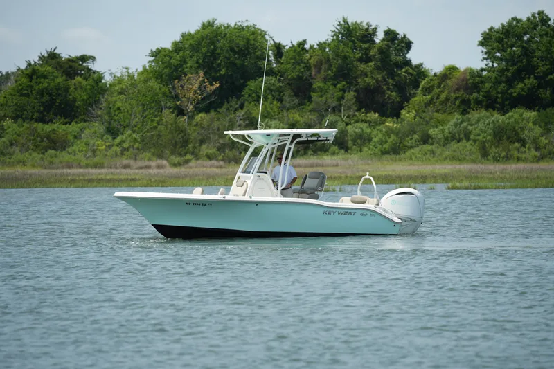 Slide: The Image of 2023 Key West 219 FS boat cruising on a calm lake with lush green trees in the background. - 10