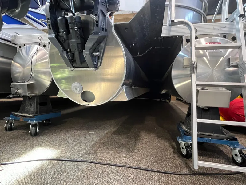 Slide: The Image of 2025 Bennington 22SXSRC pontoon boat underside with motor and ladder in a showroom. - 10