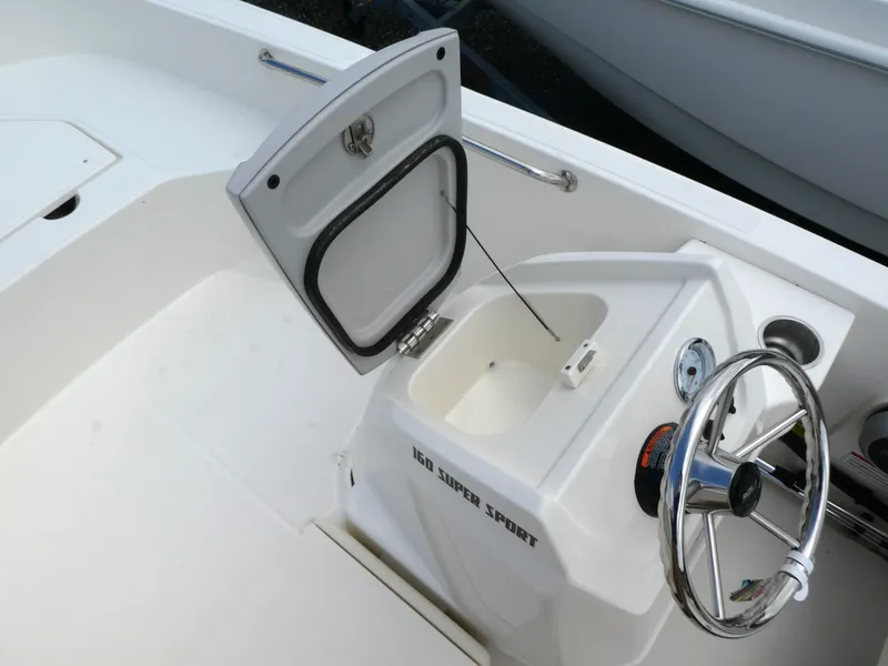 Slide: The Image of 2025 Boston Whaler 160 Super Sport boat interior with open storage compartment and steering wheel. - 11