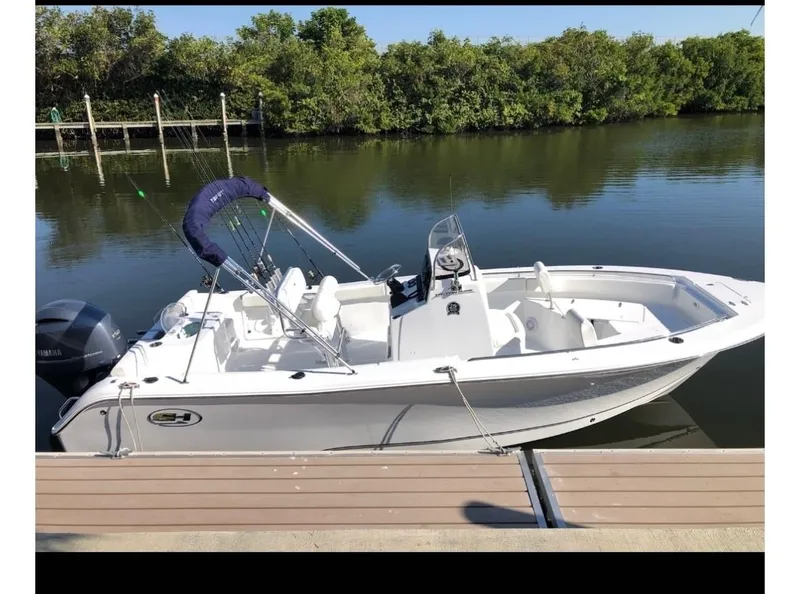 Slide: The Image of 2021 Sea Hunt Triton 225 boat docked on calm water, surrounded by lush greenery. - 4