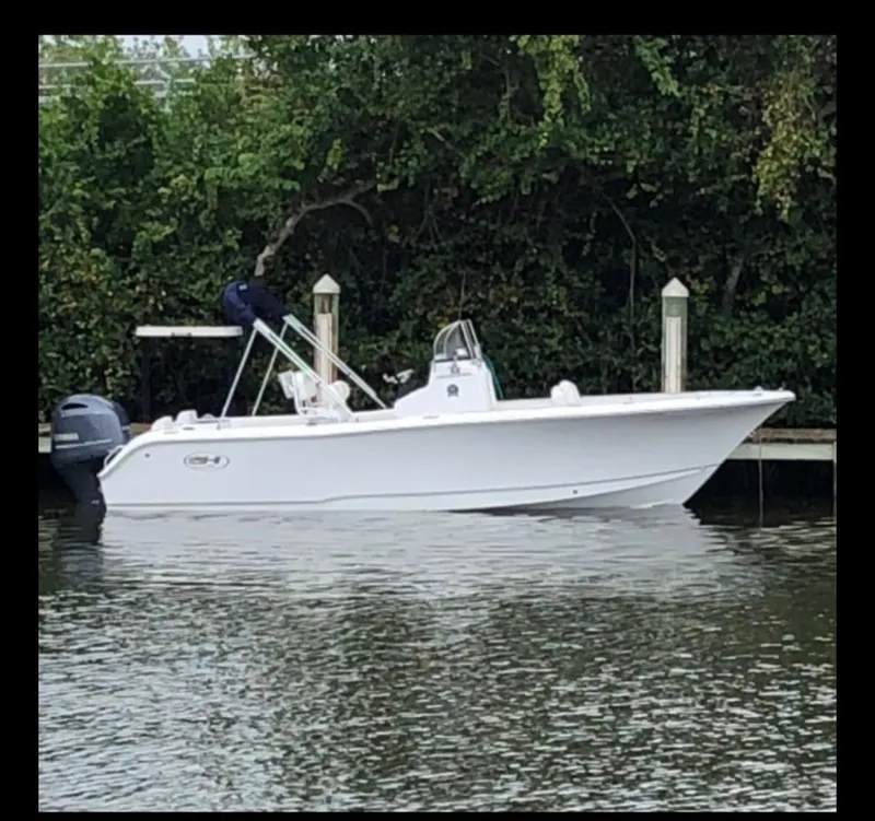 Slide: The Image of 2021 Sea Hunt Triton 225 boat docked on calm water, surrounded by greenery. - 5
