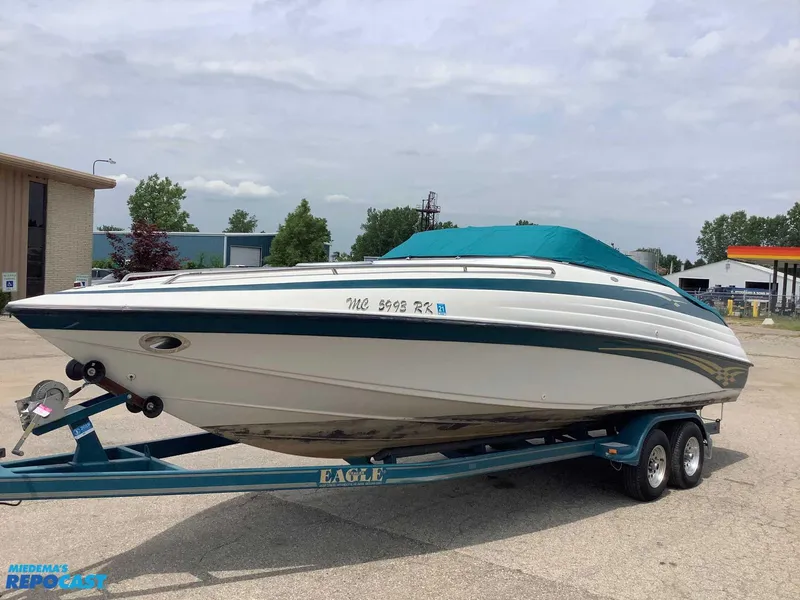 The Image of 1999 Crownline 266 CCR boat on trailer, teal cover, parked outdoors. - 1