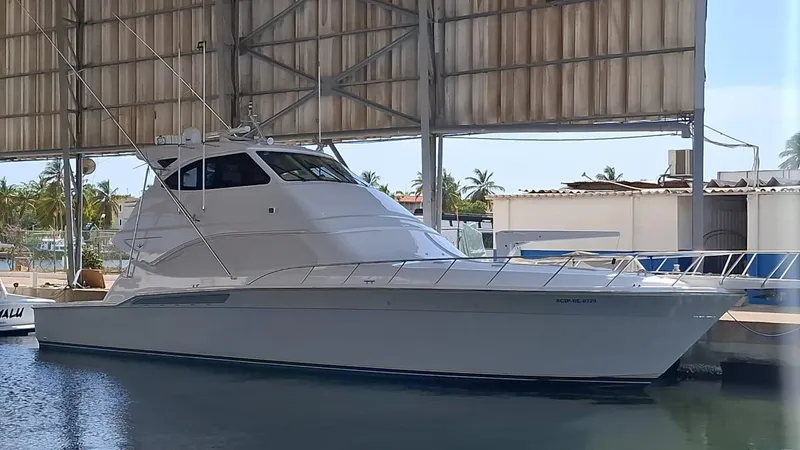 Slide: The Image of 2007 Bertram 630E yacht docked under a covered marina with palm trees in the background. - 26