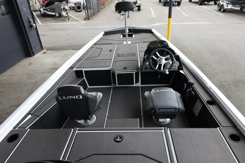 Slide: The Image of 2025 Lund 1875 Renegade SS boat interior with steering wheel and seating in a parking area. - 10