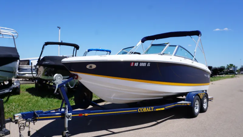 Slide: The Image of 2014 Cobalt 210 boat on trailer, parked outdoors under clear blue sky. - 0