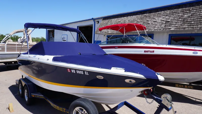 Slide: The Image of 2014 Cobalt 210 boat with blue cover on trailer, parked beside a red boat. - 46