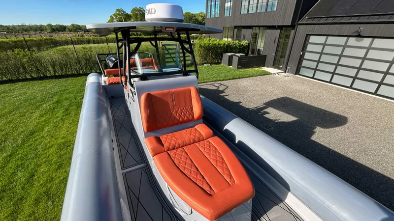 Slide: The Image of 2023 Fluid Watercraft M35 boat with orange seating, parked near a modern house. - 2