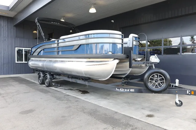 Slide: The Image of 2025 Lowe SS 230 DL pontoon boat on trailer, parked outside a building. - 2