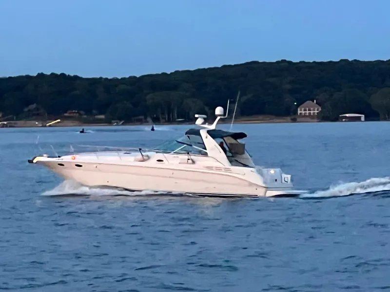 Slide: The Image of 1998 Sea Ray 400 Sundancer cruising on a serene lake with forested shoreline. - 9