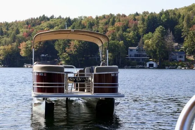 Slide: The Image of 2023 Sylvan 8522 LZ pontoon boat on a scenic lake with forested shoreline. - 2