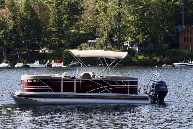 Slide: The Image of 2023 Sylvan 8522 LZ pontoon boat on a scenic lake with forested shoreline. - 3